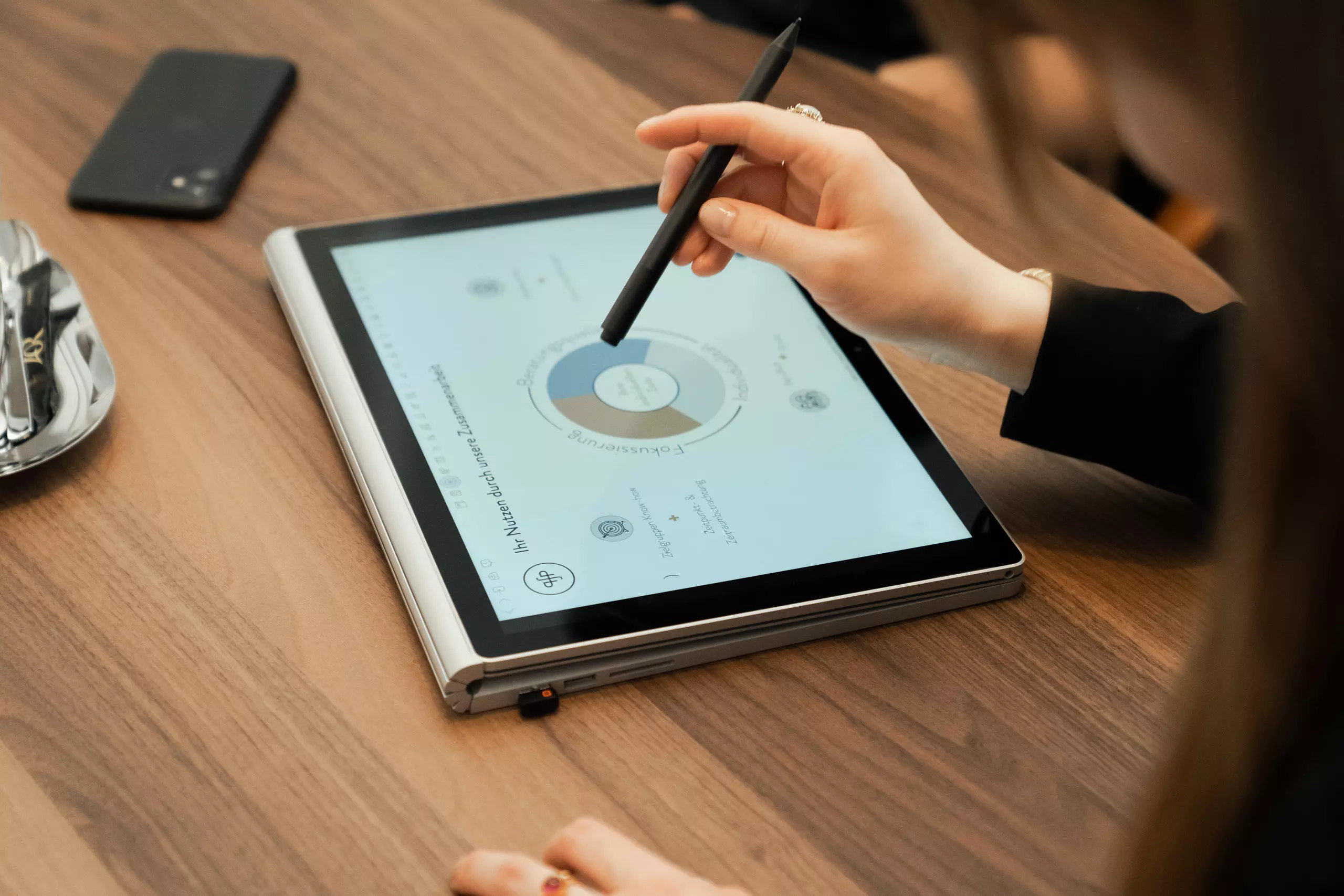 Eine weibliche Hand zeigt mit einem Stift auf eine Grafik auf einem Tablet