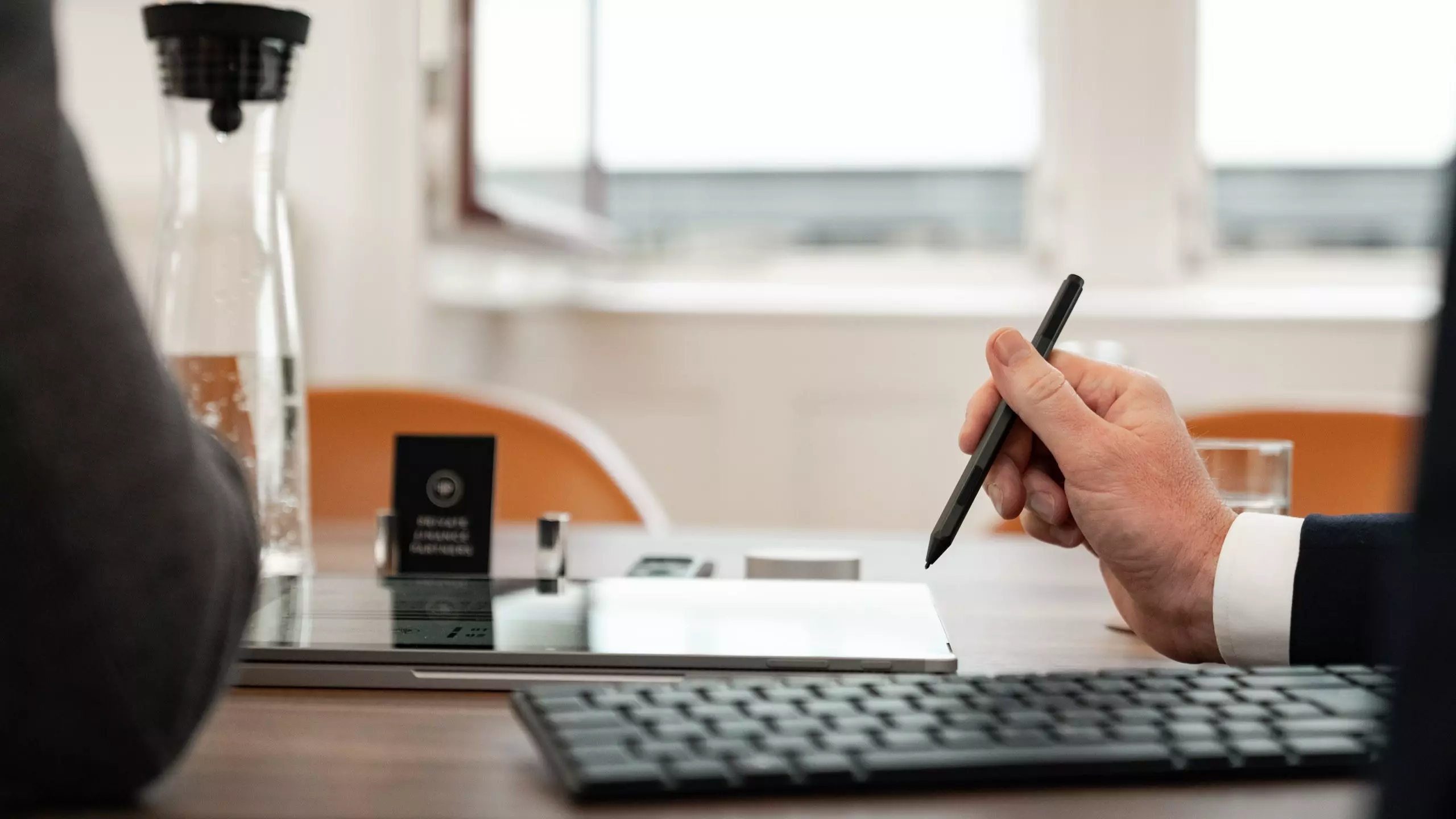 Schreibtisch mit Tastatur und Tablet auf welches von einer männlichen Hand mit einem Stift gezeigt wird