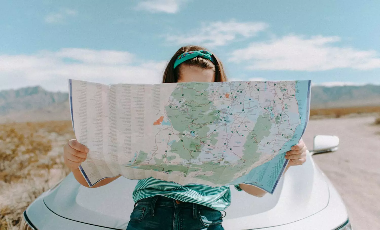 Ein Mädchen sitzt auf einer Motorhaube von einem silbernen Autor und schaut in eine Landkarte