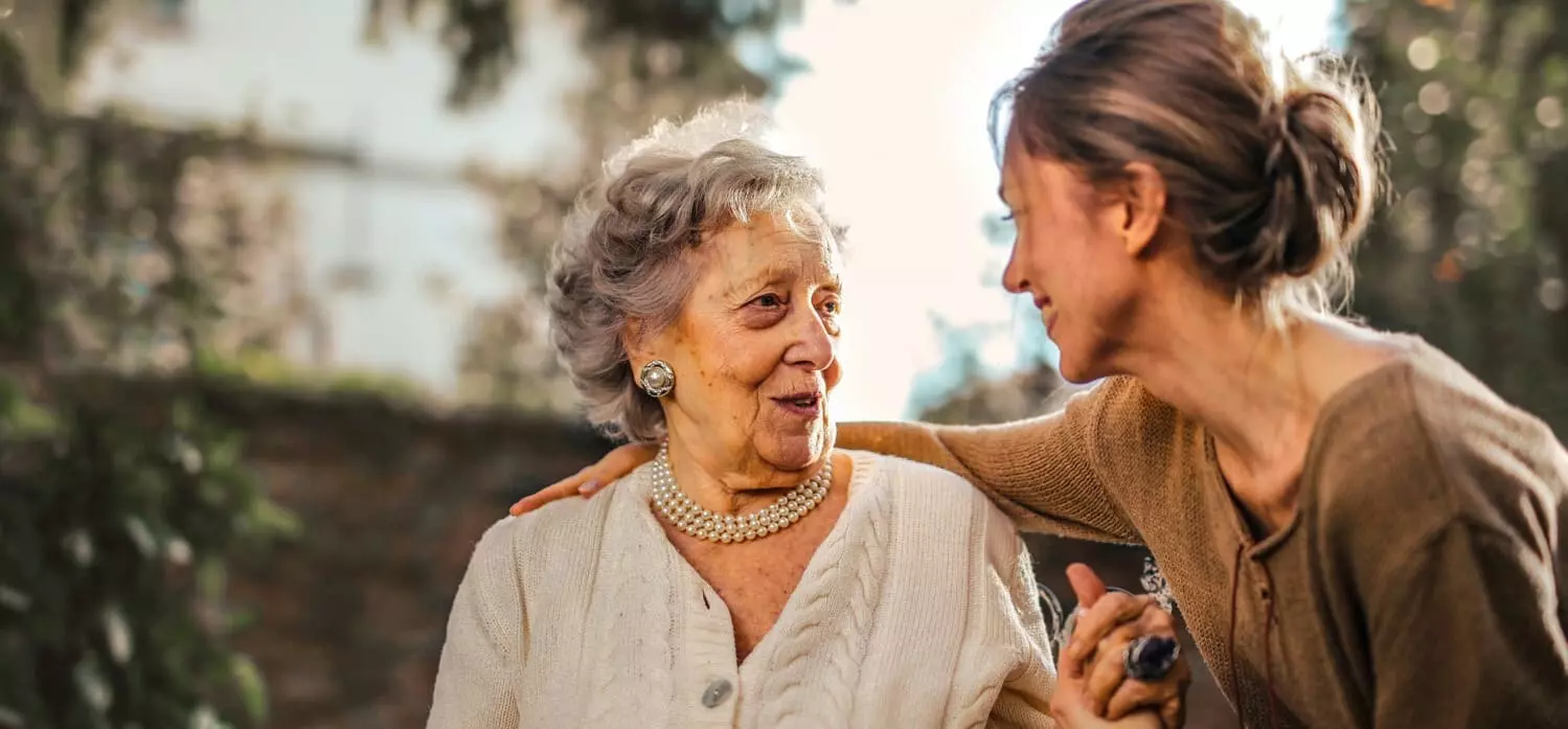 Eine Junge Frau hält ihre grinsende Großmutter im Arm und sie schauen sich gegenseitg an