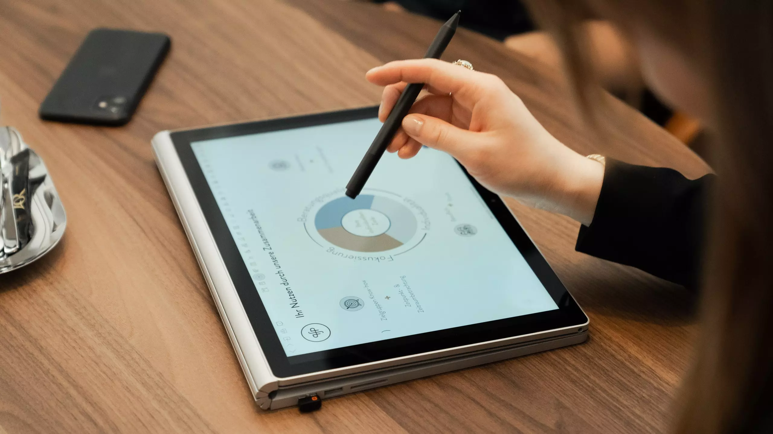Eine weibliche Hand zeigt mit einem Stift auf eine Grafik auf einem Tablet
